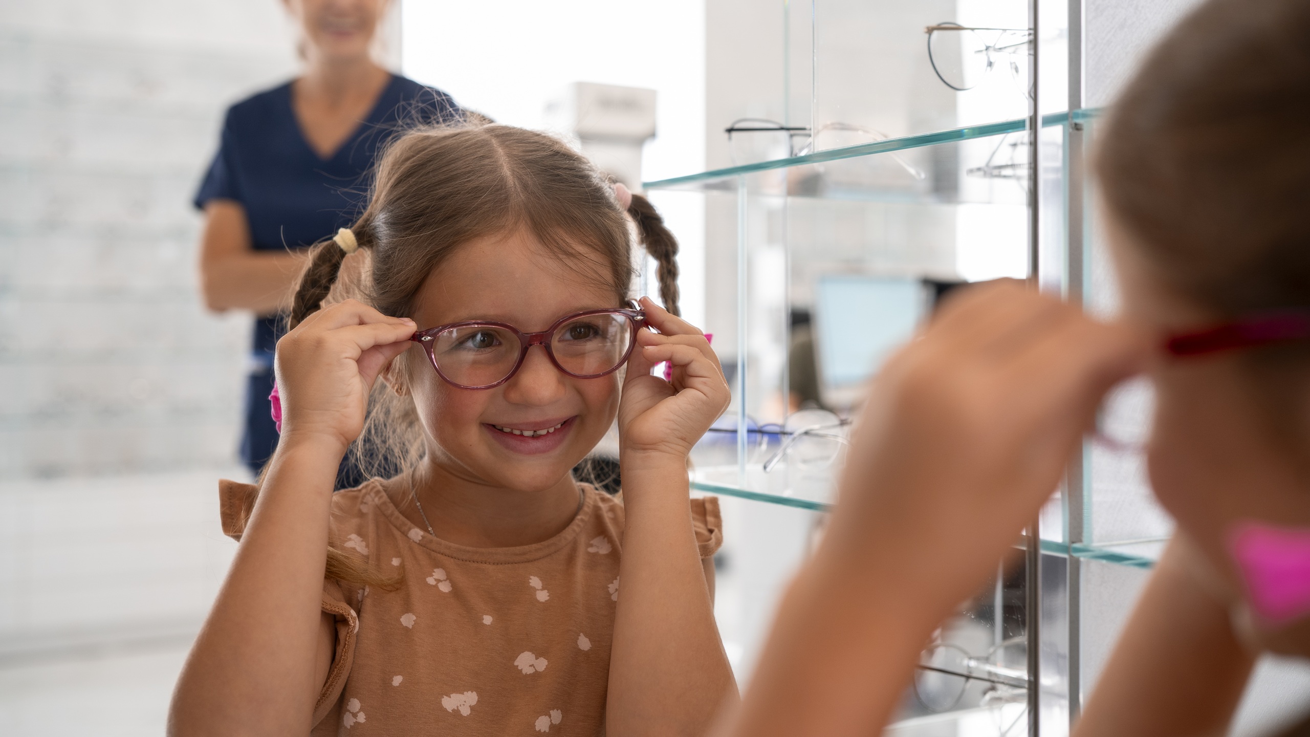 Young girl with braids trying on red eyeglasses at optometrist office