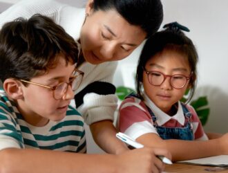 Mother helping two children with eyeglasses do homework
