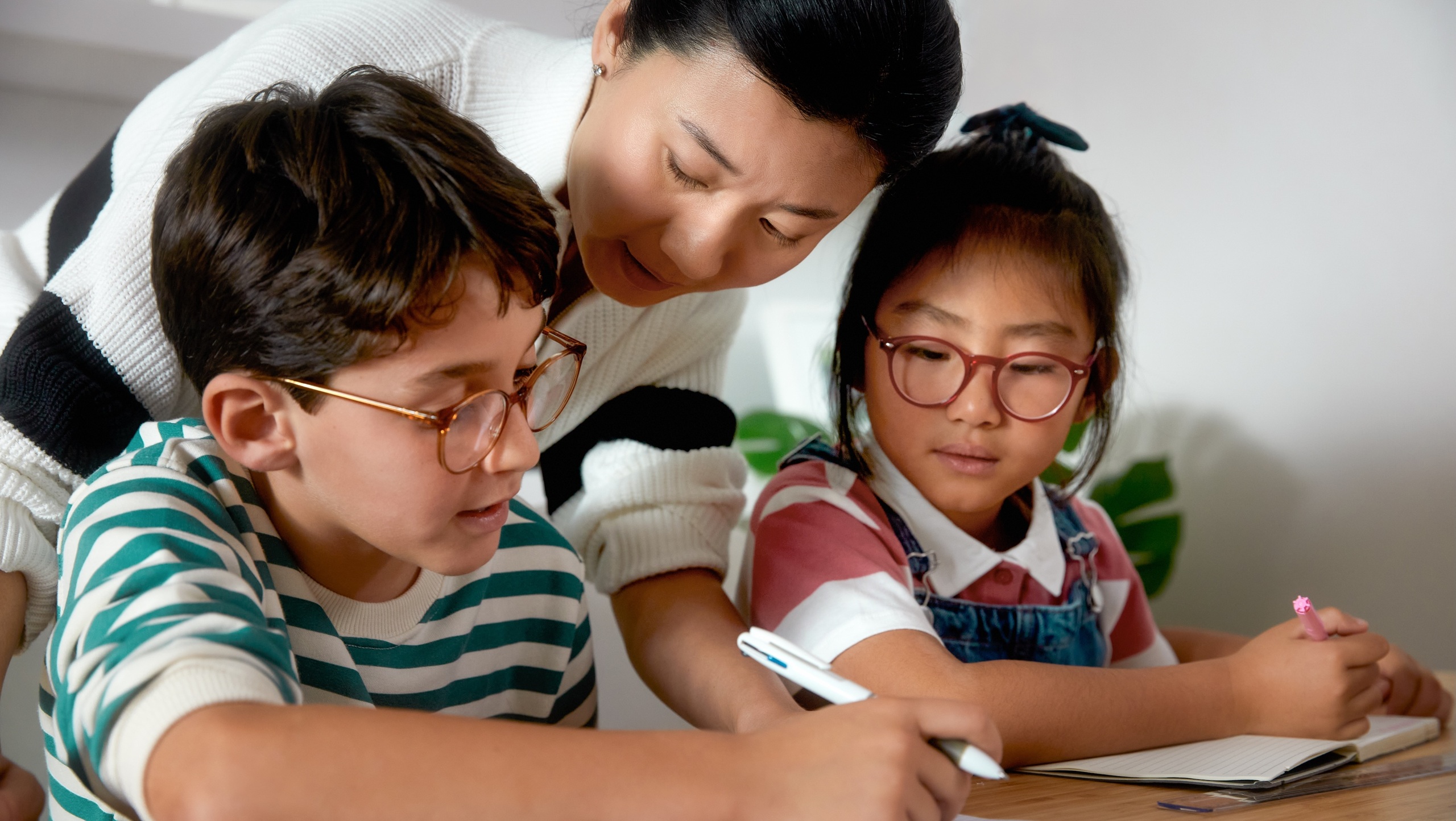 Mother helping two children with eyeglasses do homework