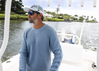 KC Scott wearing blue mirrored sunglasses and white cap on boat deck with waterfront homes visible in background