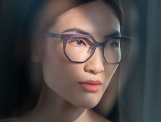 Portrait d'un mannequin portant des lunettes Blackfin avec finition iridescente en lumière naturelle de fenêtre, démontrant les propriétés changeantes de couleur des montures