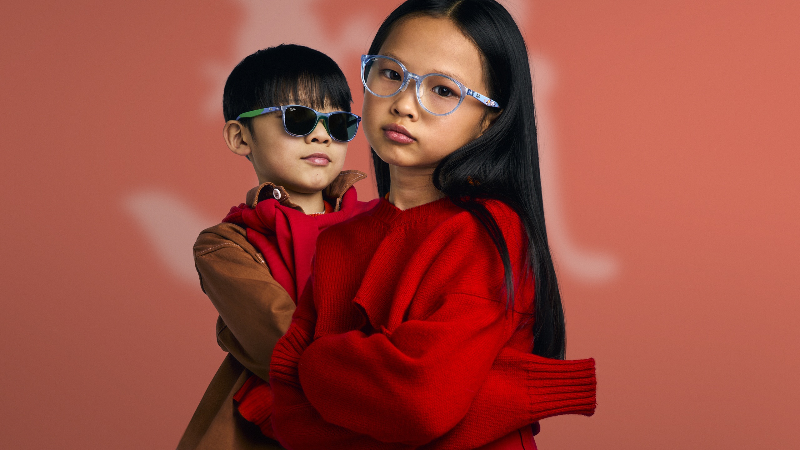 Deux enfants portant des lunettes de la collection Ray-Ban Disney Zootopia 2 sur fond dégradé rose corail ; un enfant porte des lunettes de soleil bleues transparentes avec des accents verts, l'autre porte des montures optiques bleues transparentes avec des détails orange