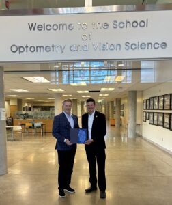Two executives holding commemorative plaque at University of Waterloo School of Optometry and Vision Science during EssilorLuxottica funding announcement