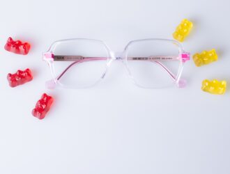 LOOKKINO 3935 eyeglasses with clear pink acetate frame and fluorescent pink temples displayed with colorful gummy bears on white background