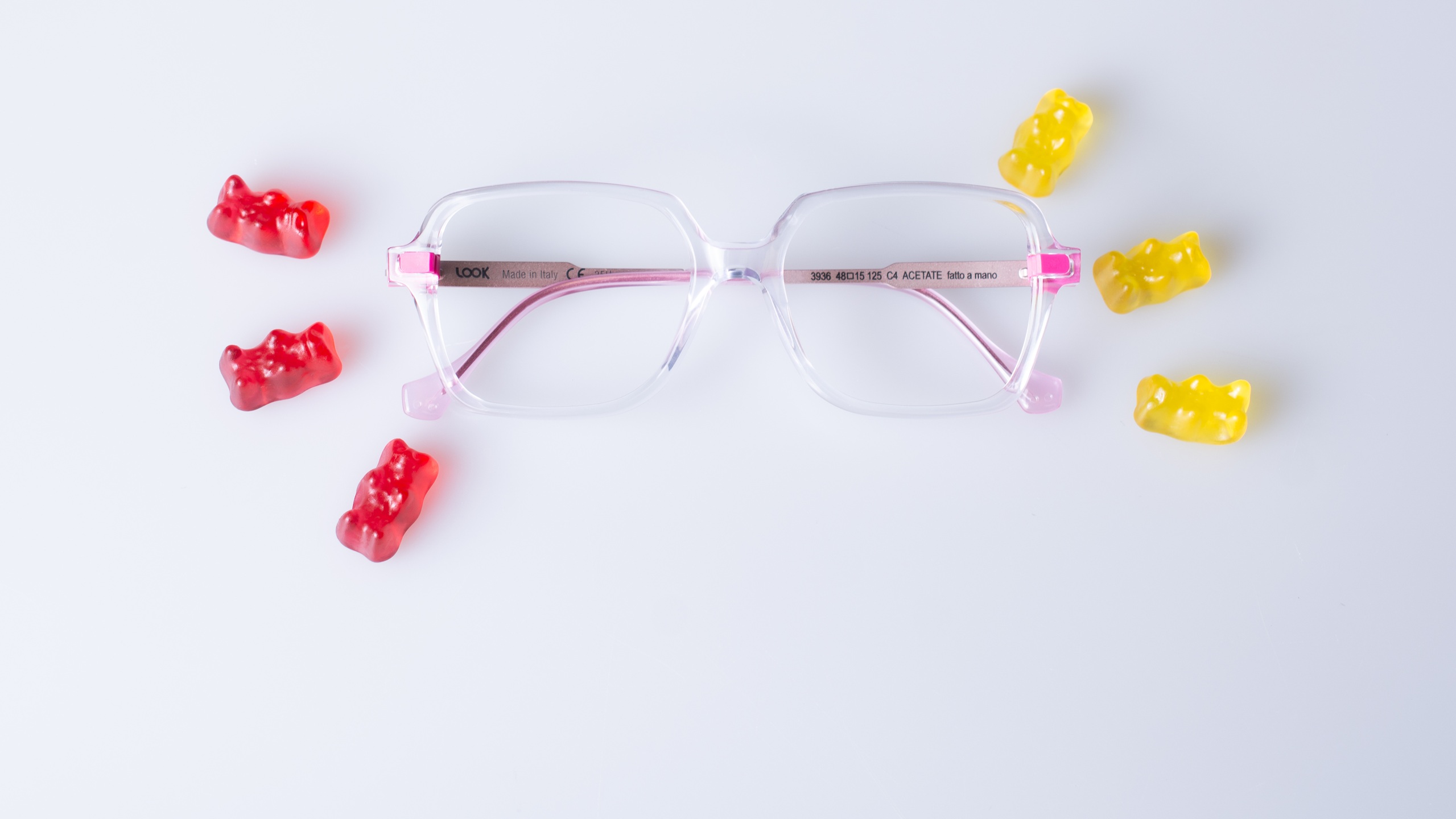 LOOKKINO 3935 eyeglasses with clear pink acetate frame and fluorescent pink temples displayed with colorful gummy bears on white background