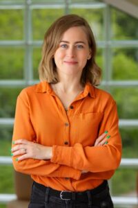 Professional headshot of Natalia Trela-McDonald, Senior Director of R&D and Technology at SightGlass Vision, wearing an orange shirt with arms crossed