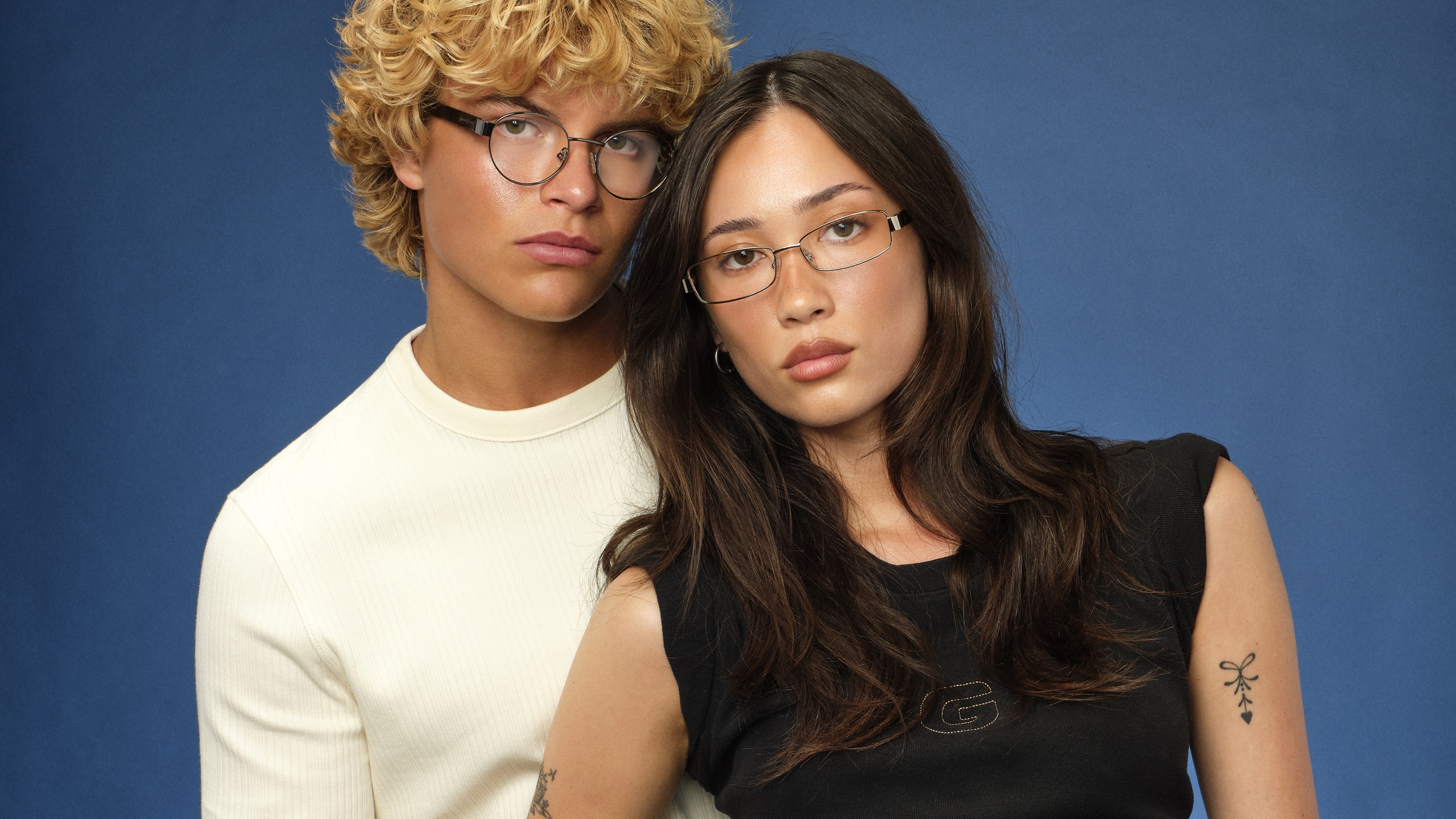 Deux jeunes mannequins portant des lunettes GUESS JEANS sur fond bleu