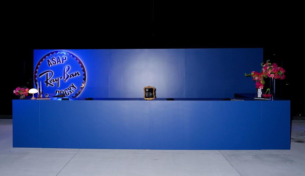 Ray-Ban Clubhouse reception desk with illuminated ASAP Rocky logo and vibrant floral arrangements