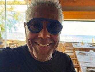 Giancarlo Esposito wearing blue Blackfin ARC-R titanium sunglasses while smiling at a beachside restaurant"