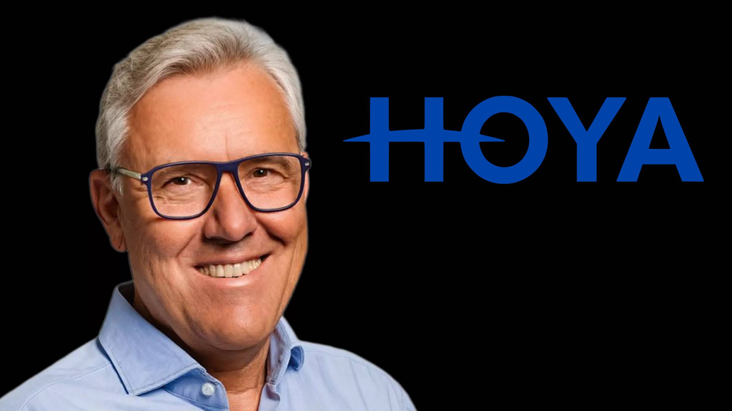 Professional headshot of a smiling executive wearing blue-framed glasses and a light blue shirt with the HOYA logo in blue letters on a black background
