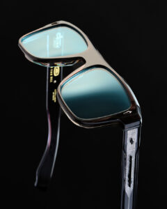 Gros plan de lunettes de soleil OTH avec monture en acétate écaille de tortue, verres miroir turquoise et détail de gravure ornementale sur la branche métallique sur fond noir