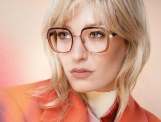 Femme aux cheveux blonds portant des lunettes carrées or rose et une veste orange