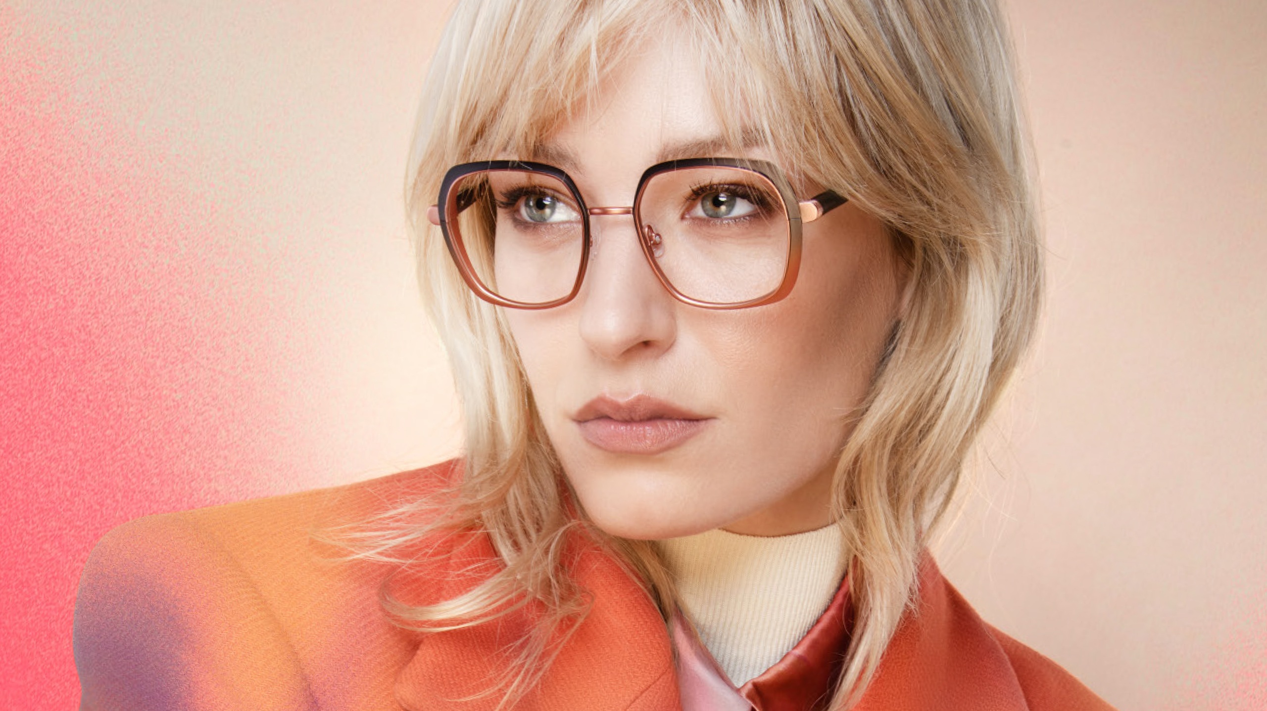 Femme aux cheveux blonds portant des lunettes carrées or rose et une veste orange
