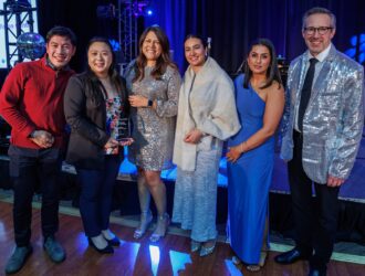 Dr. Jane Yang of Red House Vision Centre receiving OSI Group Excellence Award on stage during A Night of Winter Wonders gala with blue stage lighting