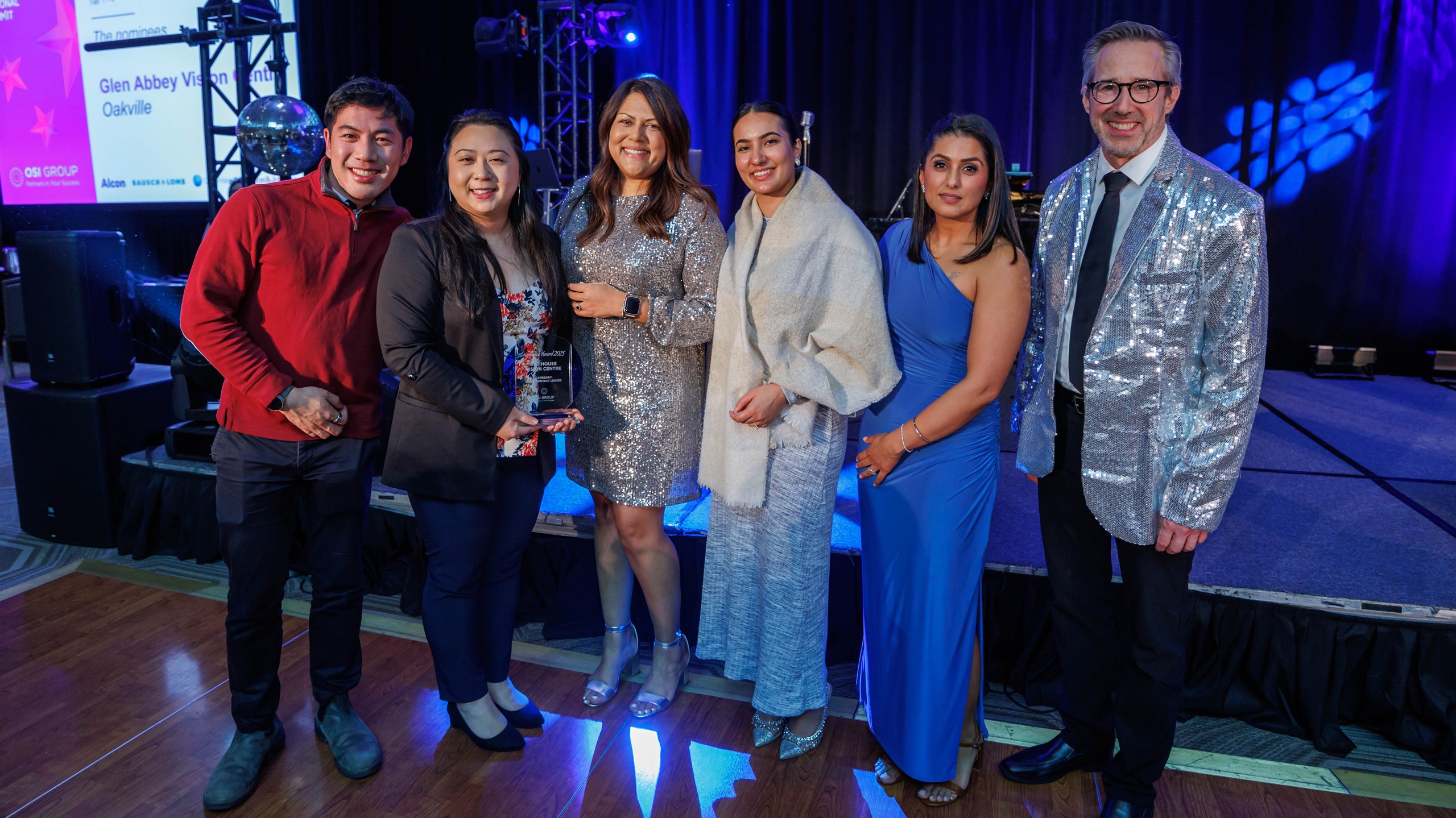 Dr. Jane Yang of Red House Vision Centre receiving OSI Group Excellence Award on stage during A Night of Winter Wonders gala with blue stage lighting