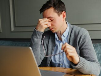 Man experiencing eye strain while working on laptop, rubbing his eyes in discomfort