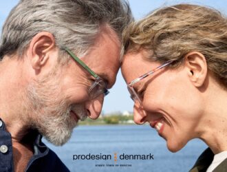 Two persons wearing ProDesign eyewear outdoors by waterfront, smiling face-to-face