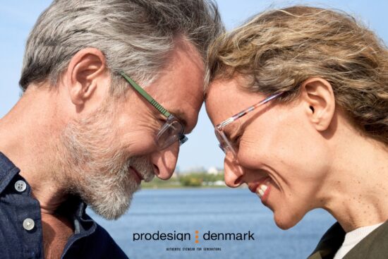 Two persons wearing ProDesign eyewear outdoors by waterfront, smiling face-to-face