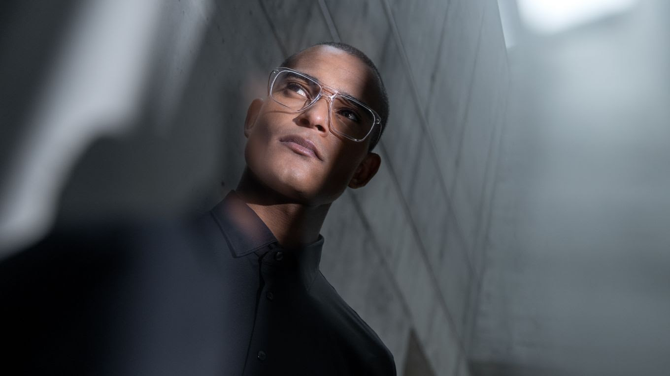 Un homme portant des lunettes Blackfin Vitra transparentes à monture carrée, regardant vers le haut dans un décor architectural minimaliste.
