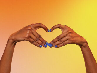 Deux mains formant un cœur sur un fond dégradé chaleureux d'orange, de rose et de jaune, avec du vernis à ongles bleu comportant des points en braille