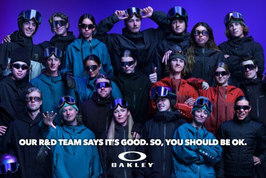 Group photo of Oakley's R&D team wearing the AURA Collection eyewear, goggles, and helmets with iridescent colourshift finish against a purple background, with text reading 'Our R&D team says it's good. So, you should be ok.