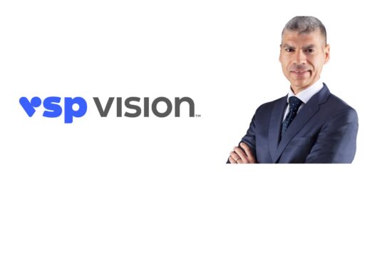 Nicola Zotta, President of Eyewear at VSP Vision, standing with arms crossed beside the VSP Vision logo