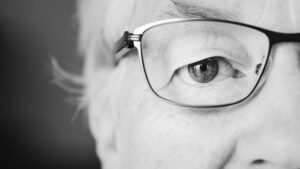 Gros plan en noir et blanc de l'œil d'une personne âgée derrière des lunettes à monture fine, mettant l'accent sur la santé visuelle.