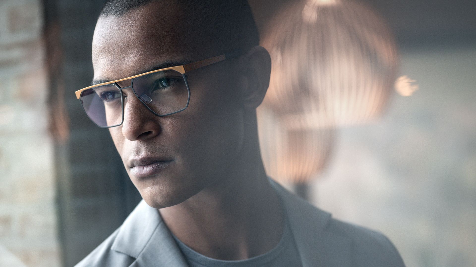 Close-up of a man wearing the Sandpoint frames, featuring a squared design with a prominent gold double bridge and blue-rimmed lenses.