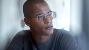 A man wearing the Stinson frames, showcasing a 1970s-inspired hexagonal shape with a clean, thin gold titanium frame.