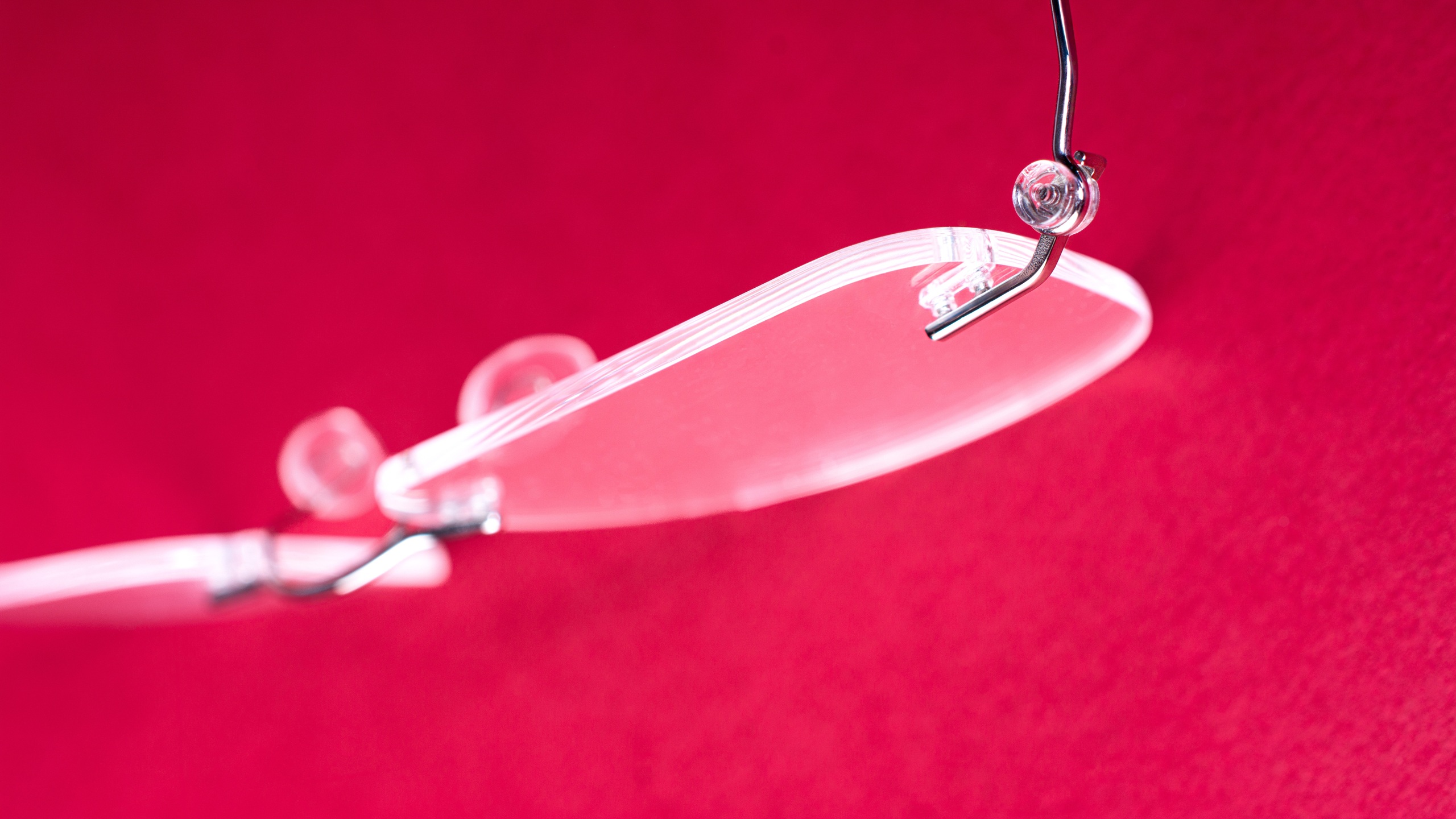 Détail en gros plan d'un verre de lunettes sans monture avec système de fixation par emboîtement, sur fond rouge.