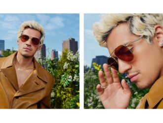 A two-panel campaign image featuring global ambassador Omar Apollo for Coach SS26. On the left, he wears a tan leather trench coat and gold aviator-style sunglasses with orange-tinted lenses, posing against a New York City skyline. On the right, a close-up highlights the sleek metal temples of the eyewear featuring the Sculpted C logo.