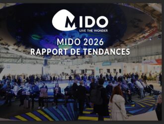 Grand hall d'exposition au salon professionnel de lunetterie MIDO 2026 avec des visiteurs rassemblés autour d'une scène circulaire éclairée en bleu. Le logo MIDO avec le slogan 'Live the Wonder' et le texte 'MIDO 2026 RAPPORT DE TENDANCES' superposés sur la scène. Stands d'exposition de marques comme Optovisol, Desio et Visionix visibles en arrière-plan.