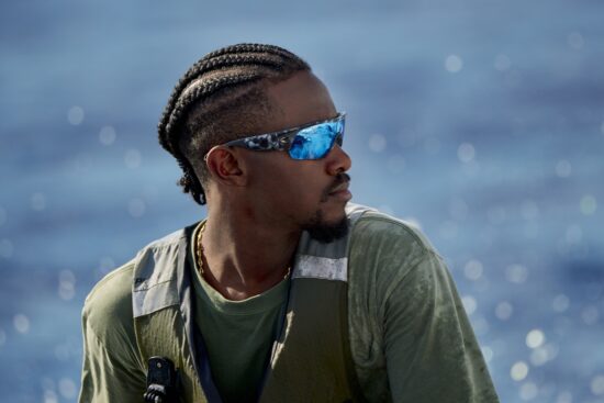 Side profile of Emmanuel Williams on the water, highlighting the high-wrap "full-screen" view and secure fit of the Pilothouse PRO sunglasses.