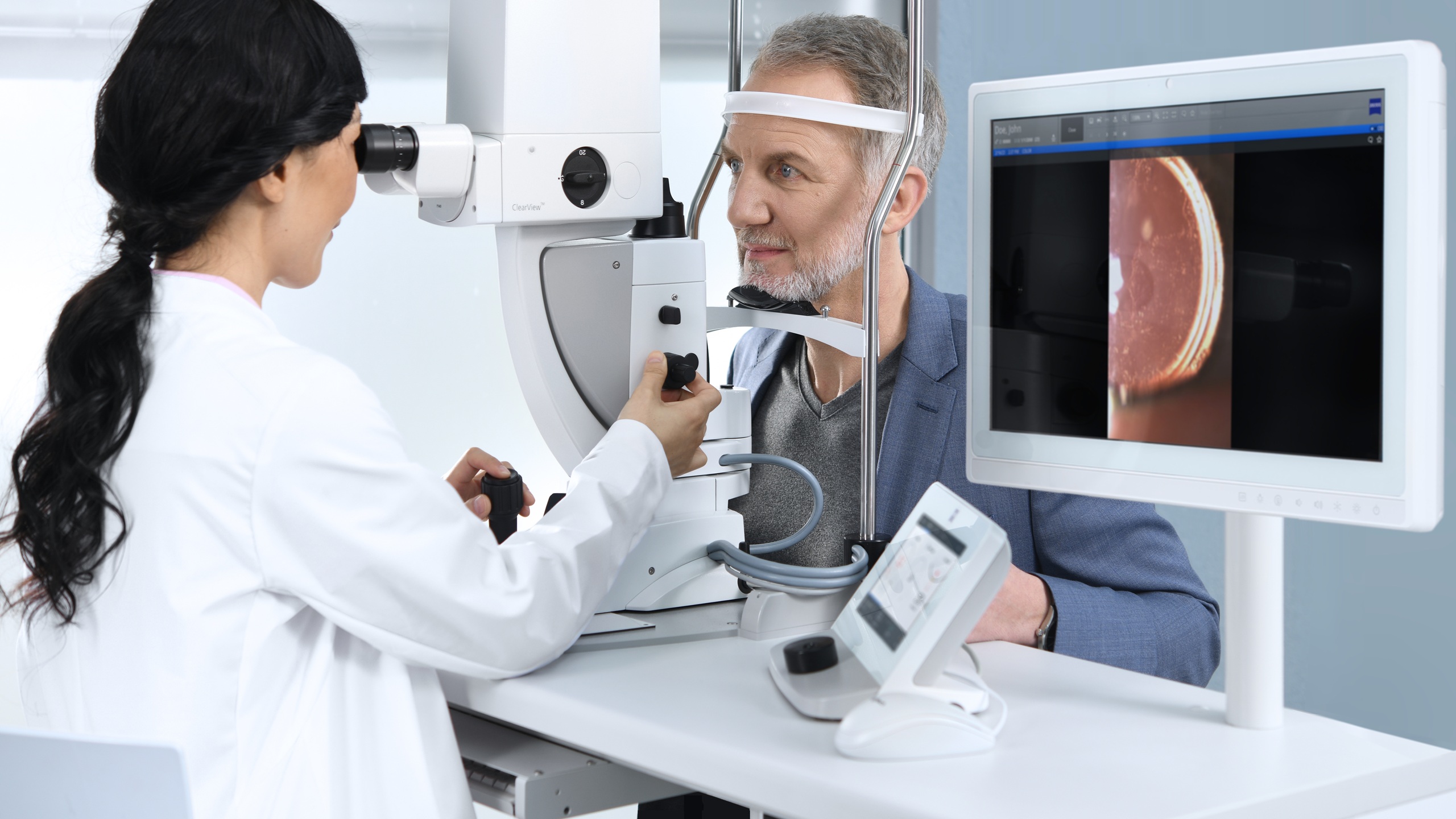 Une clinicienne utilisant le laser thérapeutique ZEISS VISULAS yag pour traiter un patient masculin, avec un moniteur affichant en temps réel une image rétinienne capturée au cours de la procédure.