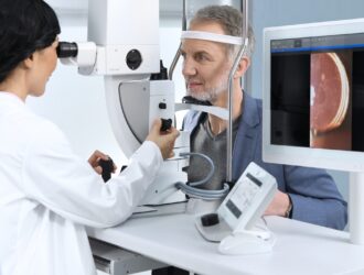 A clinician using the ZEISS VISULAS yag therapeutic laser to treat a male patient, with a monitor beside them displaying a close-up retinal image captured during the procedure.