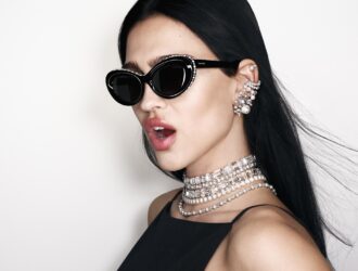 Amelia Gray portant les lunettes de soleil Swarovski SS26 à monture œil-de-chat ornée de cristaux, avec des bijoux en perles et cristaux
