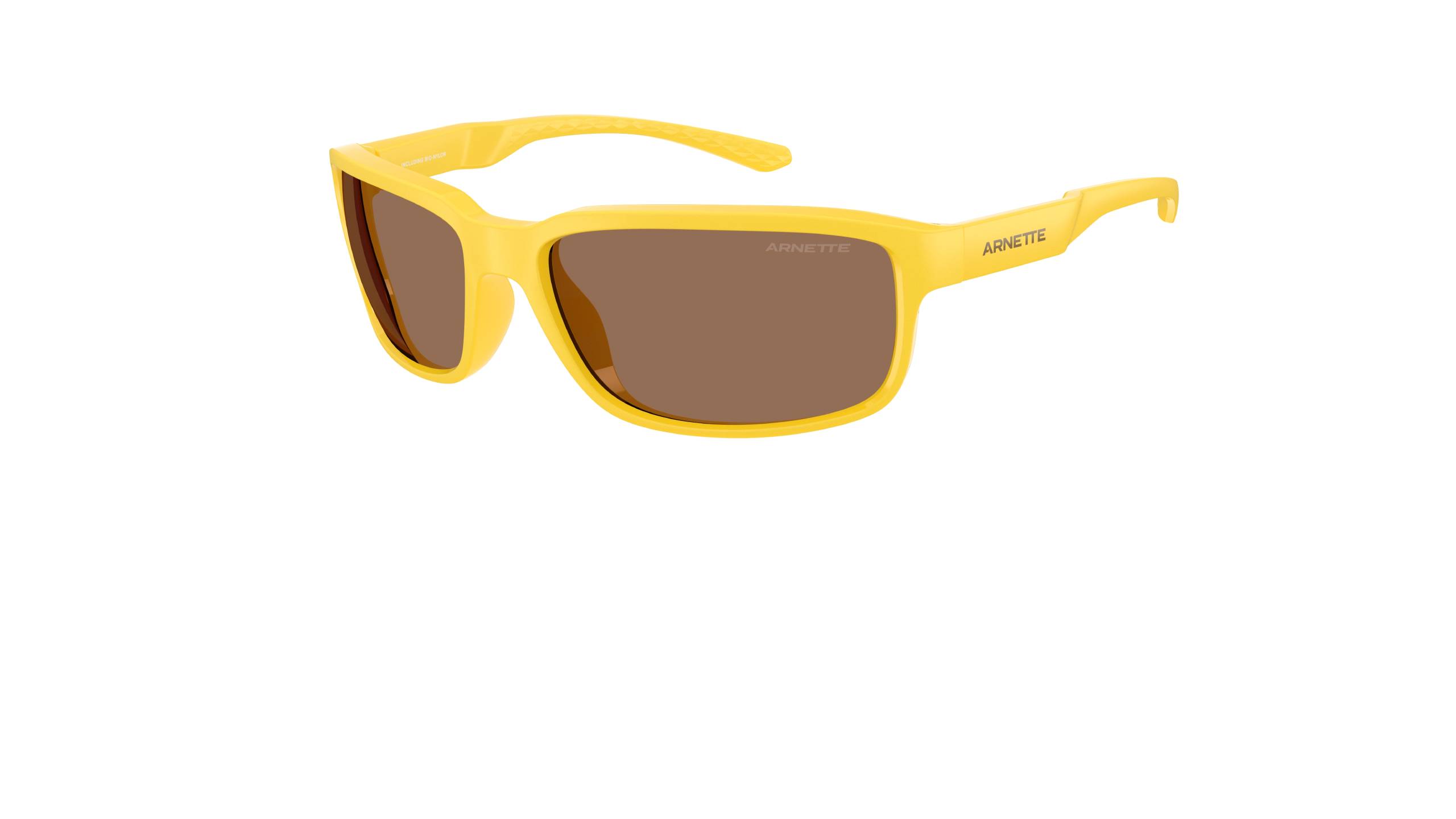 Lunettes de soleil Arnette Raven 2026 enveloppantes à monture brillante ocre/jaune vif et verres teintés marron en polycarbonate biocirculaire. Style sportif avec forme ovale biseautée, inspiré du design original des années 90 de Greg Arnette. Vue de trois quarts avec le marquage ARNETTE sur la branche.