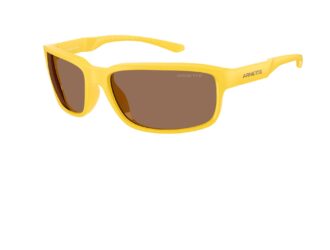 Arnette Raven 2026 wraparound sunglasses in a bold ochre/yellow glossy frame with brown tinted biocircular polycarbonate lenses. Athletic wrap style with bevelled oval shape, inspired by the original '90s design by Greg Arnette. Three-quarter view showing the ARNETTE temple branding.