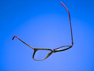 Here are some alt text options for the image, ranging from brief to more descriptive: Short: ReForm Eyewear by Mondottica — flexible black optical frames with red temple tips against a blue background