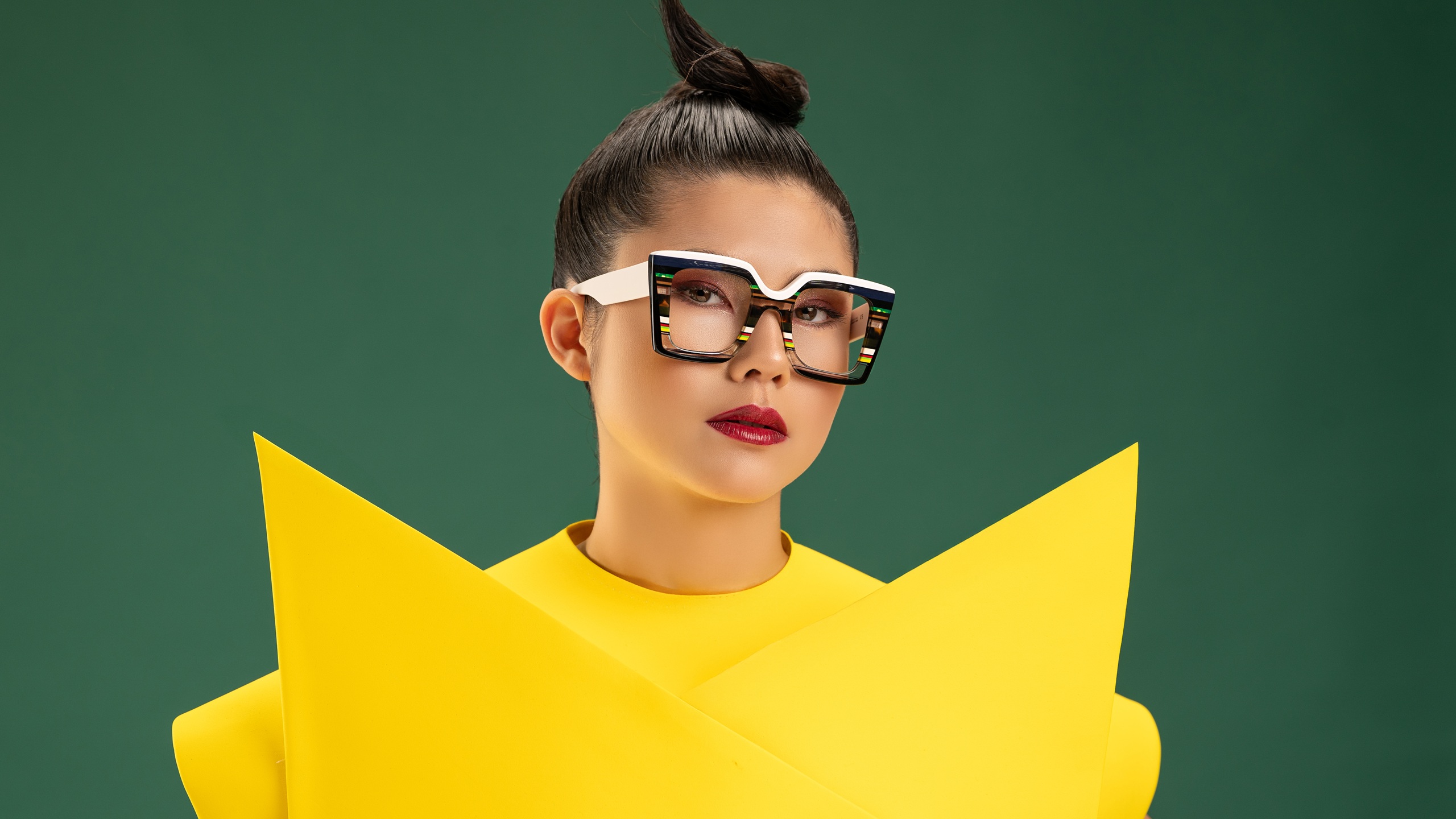 Modèle portant les lunettes optiques carrées Ultra Limited Acireale en acétate écaille et blanc avec des détails rayés multicolores, stylisée avec un haut structuré jaune vif sur fond vert profond.