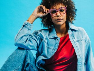 Woman wearing Spectaful LYRA optical frames in lilac, styled with a red top and denim jacket against a blue background