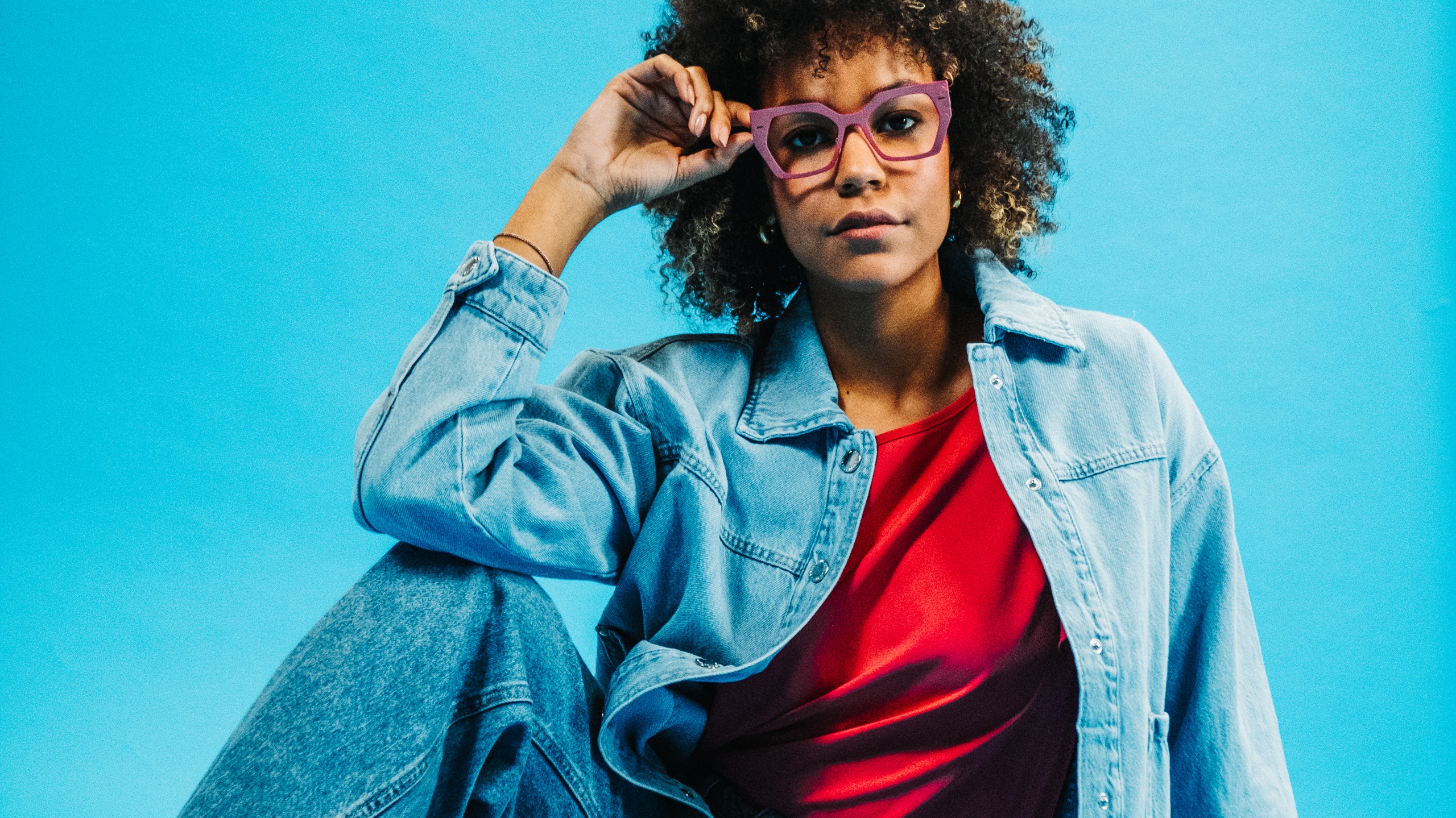 Woman wearing Spectaful LYRA optical frames in lilac, styled with a red top and denim jacket against a blue background