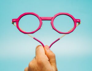 Spectaful OBSIDIAN optical frame in fuchsia polymer front held against a light blue background, temples open to reveal gold acetate detailing