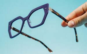 Spectaful optical frame in midnight blue polymer with geometric squared front and tortoiseshell acetate temples, held against a light blue background