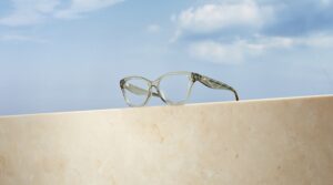 Tory Burch Kira cat-eye optical frames in translucent grey, resting on a marble ledge against a blue sky