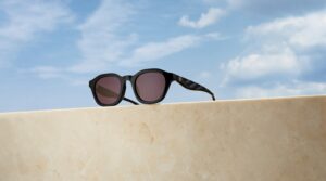 Lunettes de soleil rondes Tory Burch Kira en noir avec détail logo doré sur la branche, posées sur un rebord en marbre