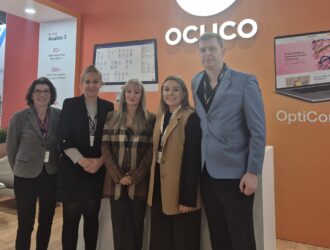 iZySolutions and Ocuco teams at the 100% Optical trade show in London, posing in front of an Ocuco "Acuitas 3" display.