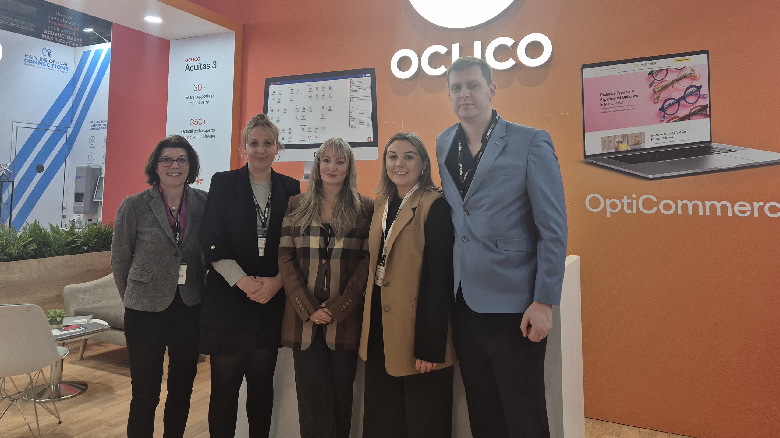 iZySolutions and Ocuco teams at the 100% Optical trade show in London, posing in front of an Ocuco "Acuitas 3" display.