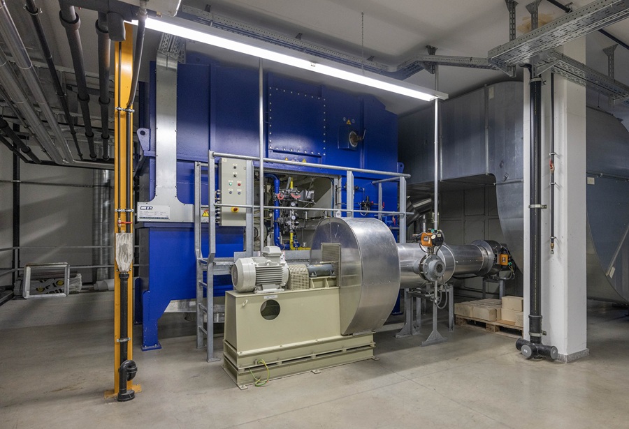 A large-scale industrial ventilation and exhaust air purification system inside the Silhouette factory. The image shows a complex setup of blue machinery, silver ductwork, and electric motors, representing the company’s transition to carbon-free production processes.