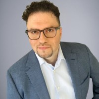 Portrait d'Ali Tafreshi, PDG de Topcon Healthcare, Inc., portant des lunettes et un veston bleu sur fond gris.